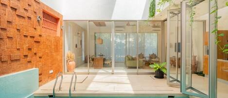 An indoor swimming pool with glass walls, a brick wall, and a seating area with a sofa and plants.