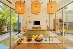 A modern living room with a sofa, a TV, wicker pendant lights, and a dining table with a placemat. - ELIVAAS Mirai Aries 3 BHK Retreat (Vagator)