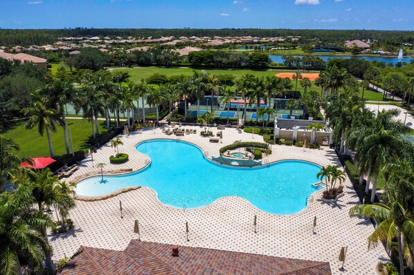 A resort with a large swimming pool, palm trees, and a golf course in the background. - Bella Terra 1st Floor unit with peaceful preserve view (Estero)