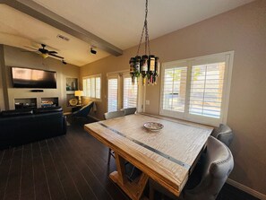 A dining area with a wooden table, chairs, a ceiling fan, a TV, and bottles on the wall. - Sunstone Escape | Pool + Hot Tub | 3BR | 9 Min to Sports Complex | $510 Free Activities (Mesquite)