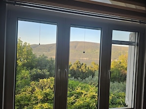 Ein Zimmer mit großen Fenstern und Blick auf einen See, Hügel und üppiges Grün.