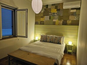 A bedroom with a bed, bedside lamps, a window with blinds, and a wall with a patchwork design. - Unique 3-bedroom apartment with AC and beautiful sea views in charming Baosici (Baosici)