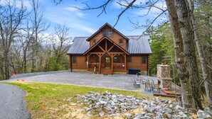 Eine Blockhütte mit Veranda, Kamin aus Stein und einer Schotterzufahrt.