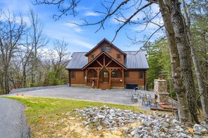 A log cabin with a porch, stone fireplace, and a gravel driveway. - 4BR, Views, Firepits, Hot Tub! (Pigeon Forge)