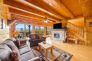 A wooden cabin interior with a stone fireplace, a sofa, a coffee table, and a television. - 4BR, Views, Firepits, Hot Tub! (Pigeon Forge)