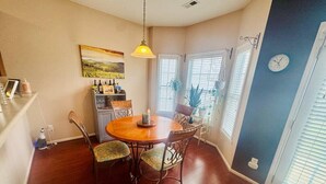 Een eetruimte met een ronde houten tafel, vier stoelen, een hanglamp en een wandklok.