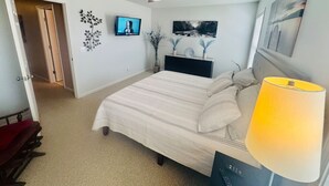 Een slaapkamer met een bed, een plafondventilator, een televisie en kunstwerken aan de muur.