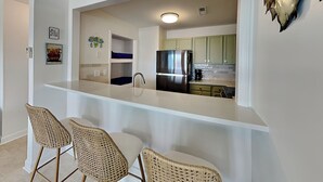 Una cocina con encimera blanca, armarios verdes, un refrigerador de acero inoxidable y una cafetera.