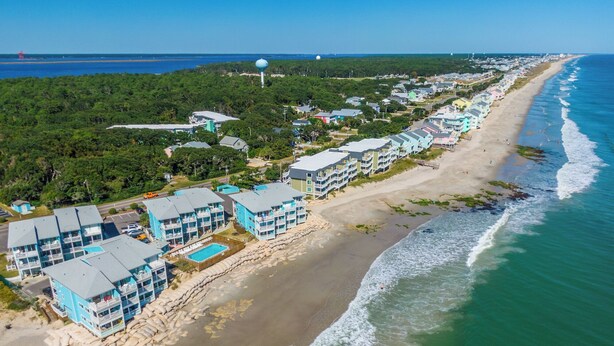 Un hotel frente al mar con varias construcciones, una playa y vistas al océano.