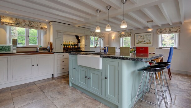 A spacious kitchen with white cabinetry, a central island with a sink, and a bar area with stools. - Drift Cottage, Salthouse, Norfolk (Salthouse)