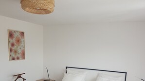 Une chambre à coucher comprenant un lit, des tables de chevet, un luminaire suspendu et une œuvre d’art accrochée au mur.
