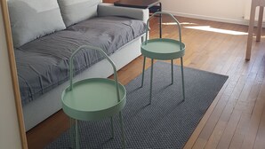 Un salon avec un canapé gris, un meuble en bois et deux fauteuils verts placés sur un tapis à motifs.