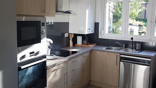 Une cuisine moderne dotée d’appareils électroménagers en acier inoxydable, de meubles en bois, d’un sol carrelé et d’une fenêtre donnant sur un paysage verdoyant.