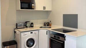 A compact kitchenette with a washing machine, microwave, toaster, and a small sink. - Bheka Guest House Parktown North, Johannesburg (Johannesburg)