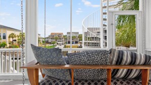 Ein Balkon mit Schaukelstuhl, gemusterten Kissen und Blick auf Wohnhäuser.