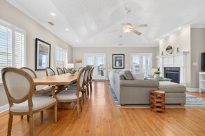 A spacious living room with a wooden dining table, chairs, a grey sofa, and a fireplace. - Shrimply Fun- 5 bedroom and 4.5 bathrooms- a private dock provides access to the deep water canal. (Ocean Isle Beach)