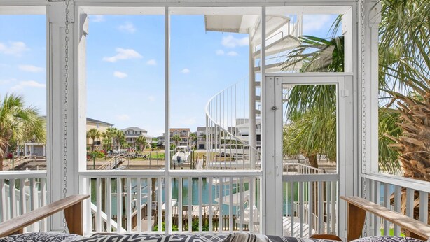 Ein Balkon mit Blick auf einen Pool und Gebäude, mit weißen Geländern und gemusterten Kissen.