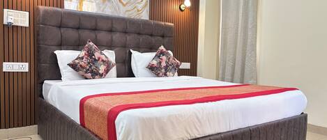 Una cama bien hecha con cabecera marrón, ropa de cama blanca y una manta decorativa roja.