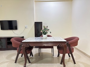 A dining area with a marble table, two chairs, a television mounted on the wall, and a flower vase. - Fortune Home Service Apartment Sector-72 (Noida)