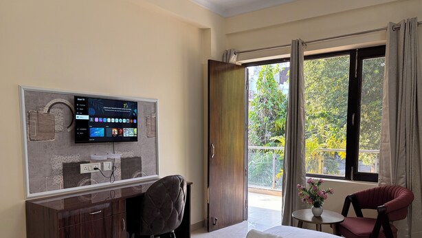 Une chambre d’hôtel comprenant un lit, un bureau avec une chaise, un téléviseur fixé au mur et un balcon donnant sur un paysage verdoyant.