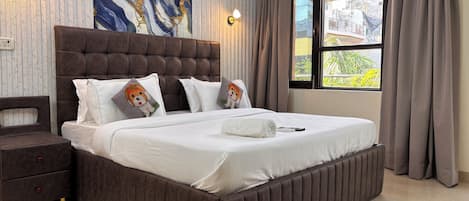 Un dormitorio con una cama grande, una mesita de noche, una lámpara de pared y una ventana con cortinas.