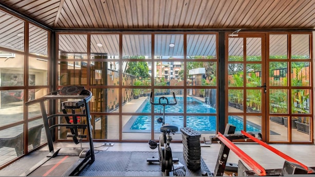 Ein Fitnessraum mit Trainingsgeräten und Blick auf ein Freibad.