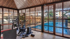 Ein Fitnessraum mit Trainingsgeräten und Blick auf ein Schwimmbad.