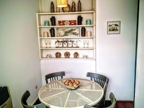 A dining area with a round table and chairs, a shelf above with decorative items, and a framed picture on the wall.
