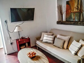 Un salon comprenant un canapé, une table basse avec un saladier, un téléviseur fixé au mur et une lampe sur une table d’appoint.