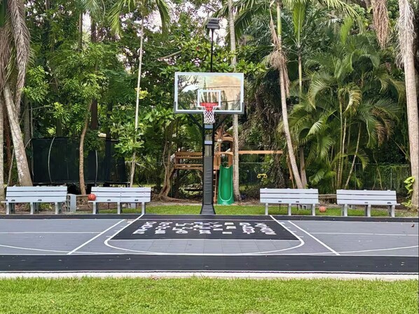 Una cancha de baloncesto con aro, bancos y un tobogán.