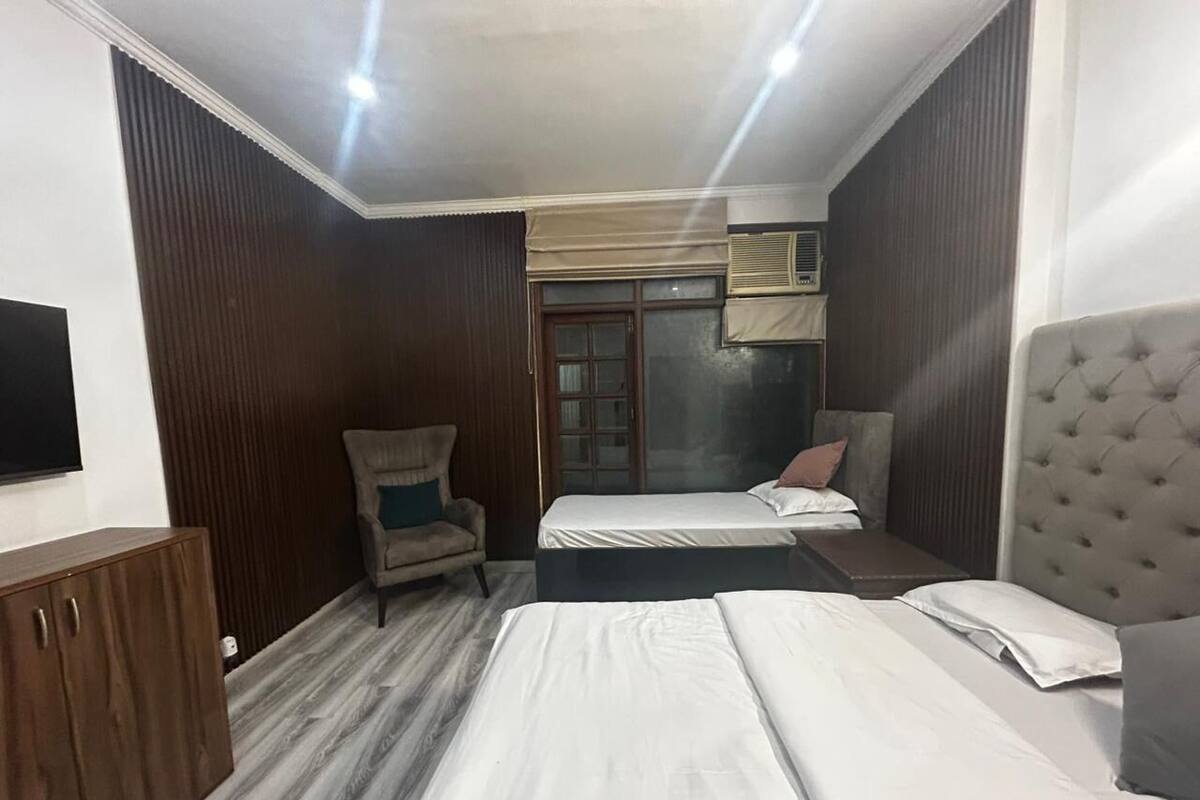 Habitación de hotel con una cama grande, una cama más pequeña, una silla, un armario y una ventana con persianas.