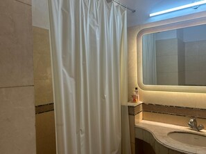 A bathroom with a shower curtain, a mirror, a sink, and a bottle of hand soap. - The Hideout GK (New Delhi)