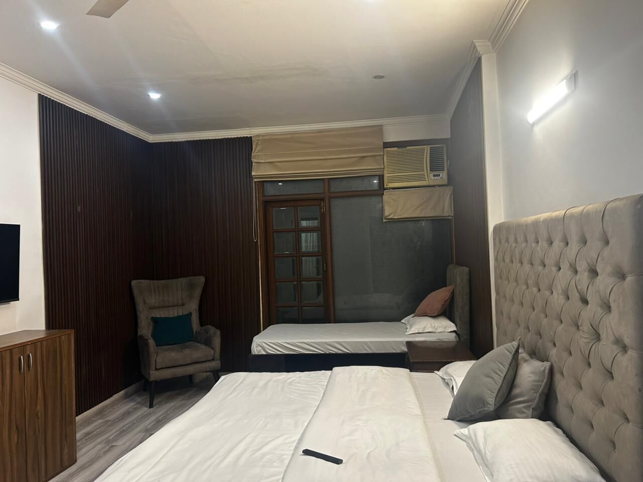 Un dormitorio con dos camas, un armario de madera, una silla y un ventanal con cortinas.