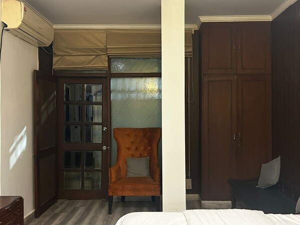 A hotel room with a bed, a wooden wardrobe, a glass door, and a chair. - The Hideout GK (New Delhi)
