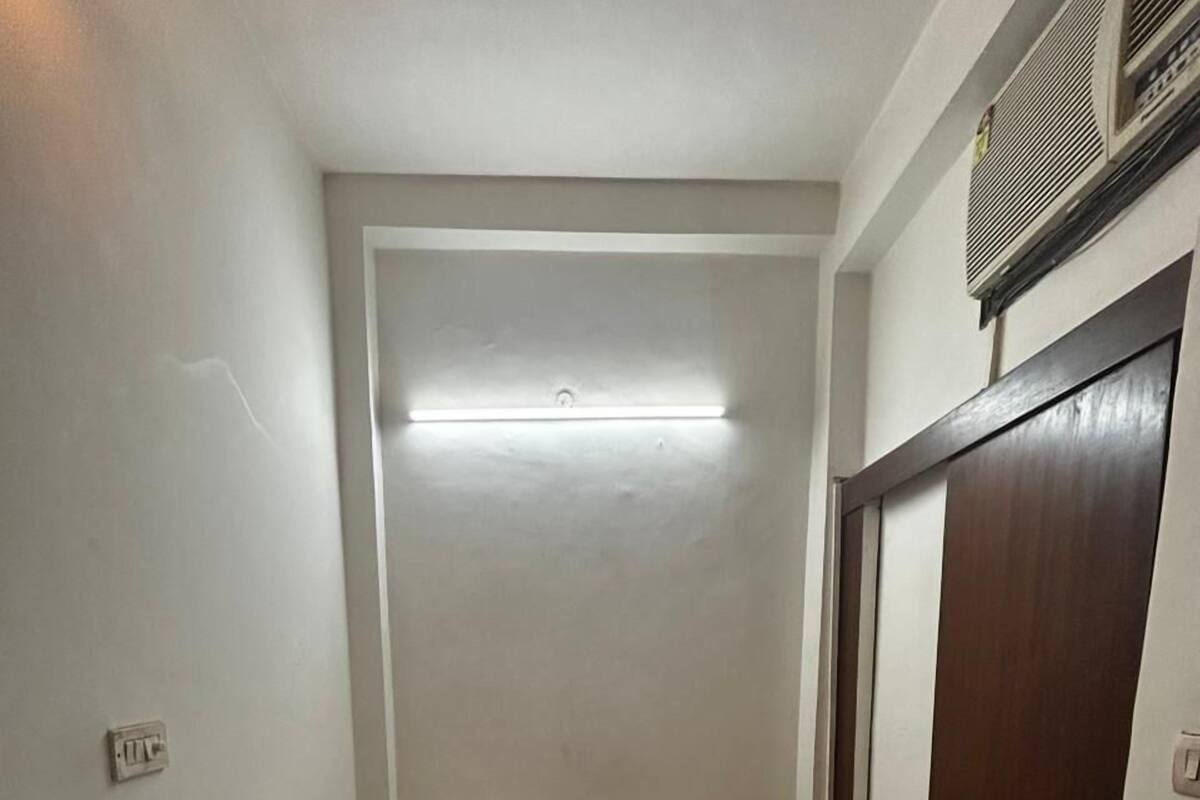 Una habitación pequeña y estrecha con una cama individual, una mesita de noche, un armario de madera y una lámpara en el techo.