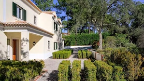 A building with a tiled roof, a paved pathway, and neatly trimmed hedges. - Villa in Quinta do Perú Golf & Country Club (Quinta do Conde)