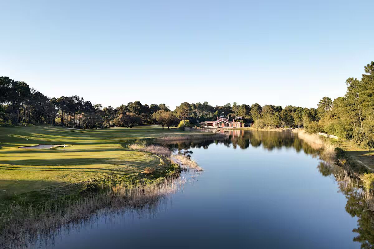 Un parcours de golf avec un étang, un club-house et des arbres environnants.