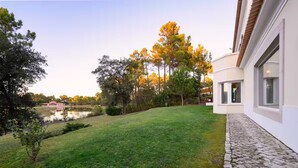 A modern house with a stone pathway, a grassy lawn, and trees with autumn foliage. - Villa in Quinta do Perú Golf & Country Club (Quinta do Conde)
