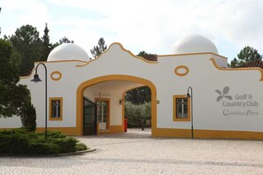 A building with a white and yellow facade, an arched entrance, and a sign for 'Golf & Country Club Quimby Peru.' - Villa in Quinta do Perú Golf & Country Club (Quinta do Conde)