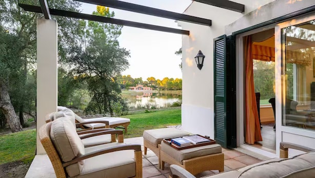 A covered patio with wicker furniture, a table, and a view of a lake and trees. - Villa in Quinta do Perú Golf & Country Club (Quinta do Conde)