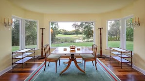 A dining room with a table and chairs, large windows with a view of a golf course, and a chandelier. - Villa in Quinta do Perú Golf & Country Club (Quinta do Conde)