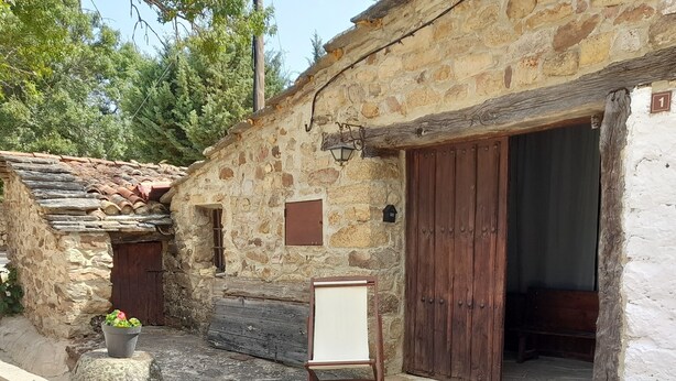 A rustic stone building with a wooden door, a small window, and a signboard on the ground. - THE SHELTER OF MOLINOS DE RAZÓN (Molinos de Razón)