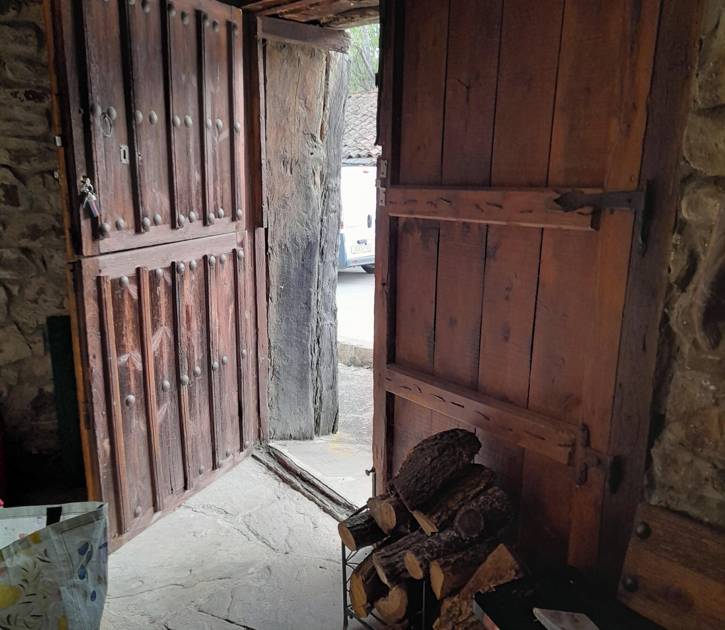 Een houten deur in landelijke stijl met een metalen grendel, een stenen muur en een kleine opening naar buiten.