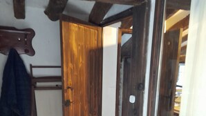 A wooden door with a latch, a coat hanging on a rack, and a mirror reflecting part of the room. - THE SHELTER OF MOLINOS DE RAZÓN (Molinos de Razón)