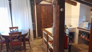 A rustic interior with a wooden dining table, chairs, a kitchen area with a sink and shelves, and a stone floor. - THE SHELTER OF MOLINOS DE RAZÓN (Molinos de Razón)