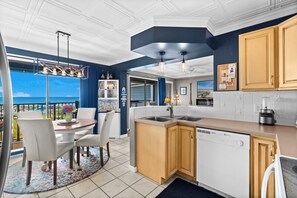 A modern kitchen with a view to the sea, featuring a dining area with a table and chairs, and a kitchen island with a dishwasher. - 2 BR Ocean View Condo | Myrtle Beach Resort A0527 (Myrtle Beach)