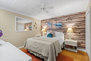 A bedroom with a wooden wall, a ceiling fan, a bed with a quilt, two bedside tables with lamps, and a bookshelf. - 2 BR Ocean View Condo | Myrtle Beach Resort A0527 (Myrtle Beach)