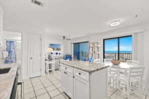 A spacious kitchen with a large island, white cabinetry, and a view of the ocean through a large window. - Ocean View 2 BR Condo: Myrtle Beach Resort B0546 (Myrtle Beach)