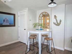 A room with a white door, a round table with stools, a wall-mounted mirror, and a framed picture. - 2BR Tower Ocean View | Myrtle Beach Resort RT2114 (Myrtle Beach)
