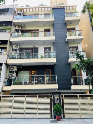 A multi-story residential building with balconies, air conditioning units, and a gated entrance. - Fortune Home Service Apartment 4BHK J191 (New Delhi)